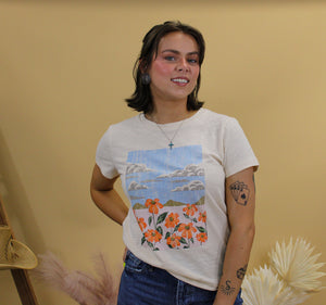 Model is wearing the jade graphic tee featuring a nature landscape. Model is standing in front of a western inspired back drop. 