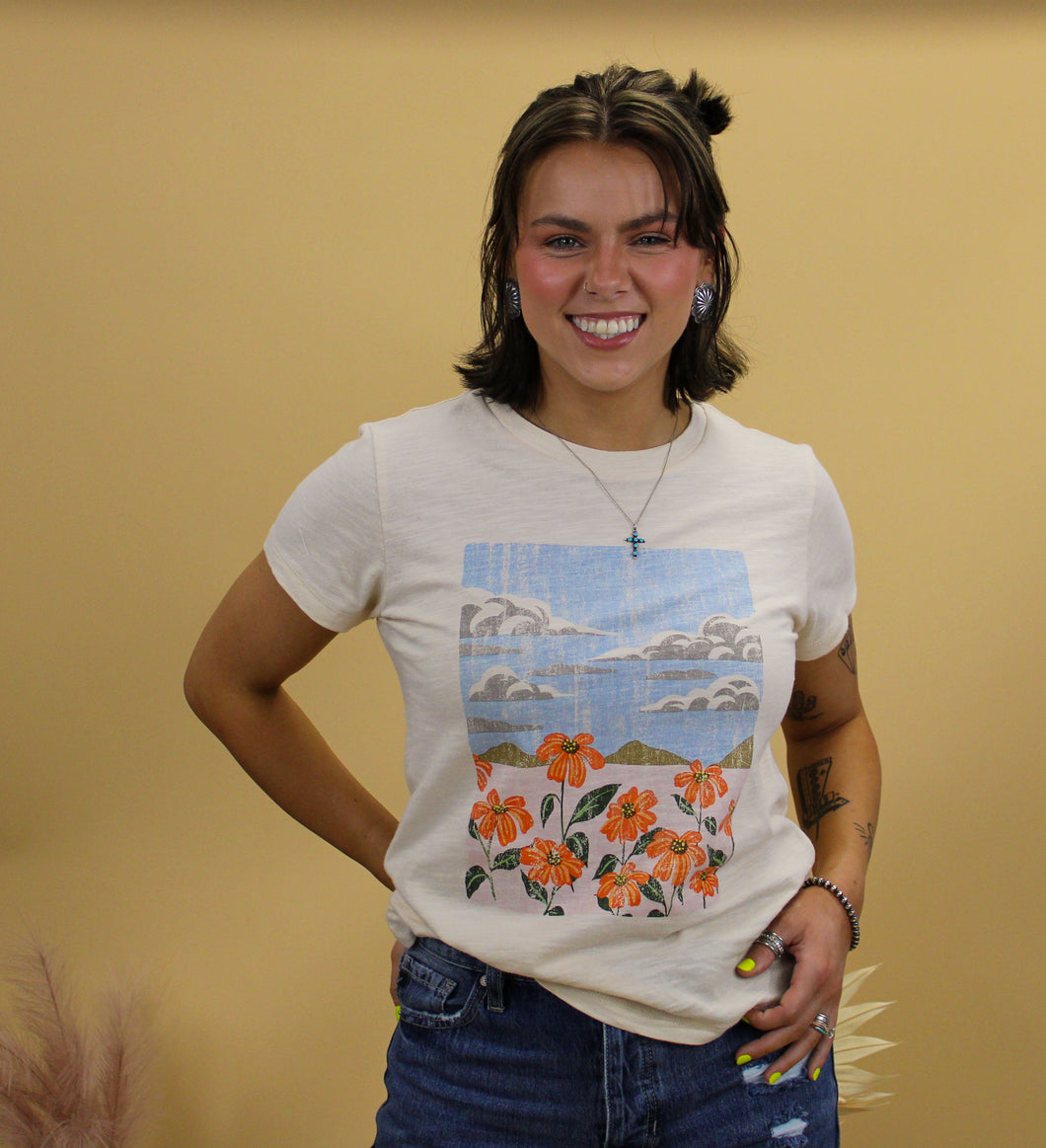 Model is wearing the jade graphic tee featuring a nature landscape. Model is standing in front of a western inspired back drop. 