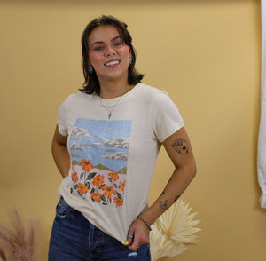 Model is wearing the jade graphic tee featuring a nature landscape. Model is standing in front of a western inspired back drop. 