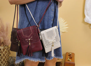 Image shows a faux leather crossbody bag with tassle in a western style, available in four colors, brown, burgundy, black and cream. 