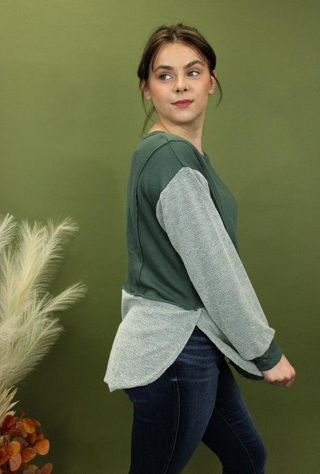 Model is wearing a green and grey colorblock long sleeve top 