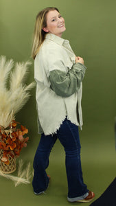Model is wearing a green, teal, and cream color block shacket in front of a fall themed backdrop. 