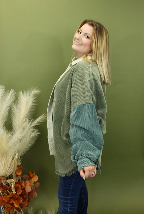 Model is wearing a green, teal, and cream color block shacket in front of a fall themed backdrop. 