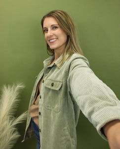 Model is wearing a moss green corduroy jacket in front of a fall backdrop 