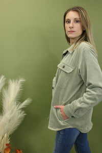 Model is wearing a moss green corduroy jacket in front of a fall backdrop 