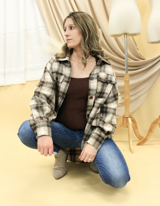 Model is wearing a brown and cream flannel button up shirt. 