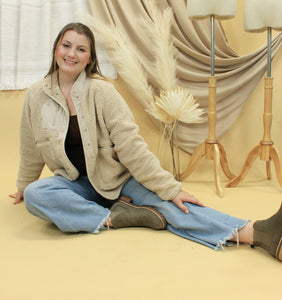 Model is wearing a neutral color sherpa jacket in front of a neutral backdrop. 