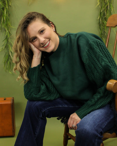 Model is wearing a green sweater in front of a festive background. 