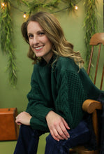 Load image into Gallery viewer, Model is wearing a green sweater in front of a festive background. 
