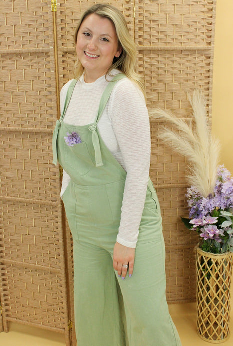 Model is wearing a light green overall with a white long sleeve top. 